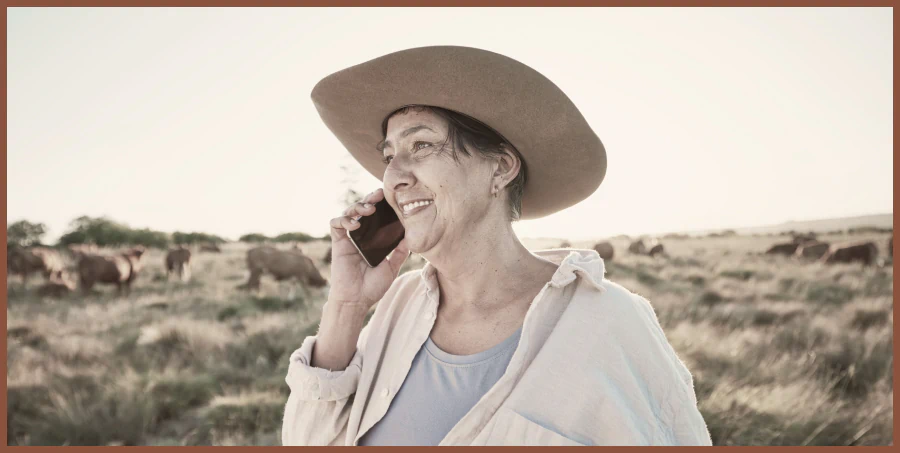 Rancher in a wide-brim hat talking on the phone in a cattle pasture