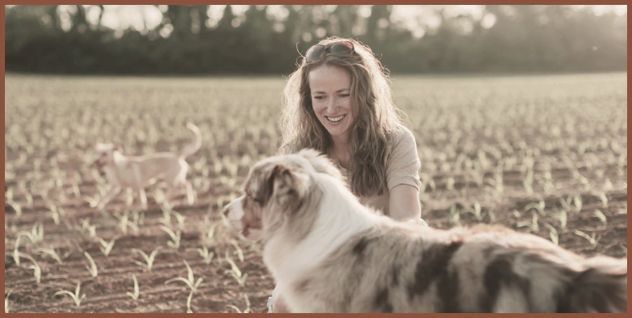 Team member smiling in a field with an Australian shepherd